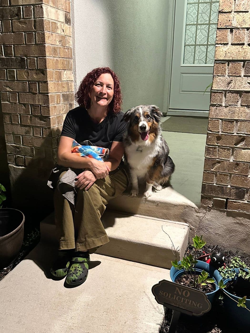 A smiling owner sitting on her front step next to her blue merle Australian shepherd