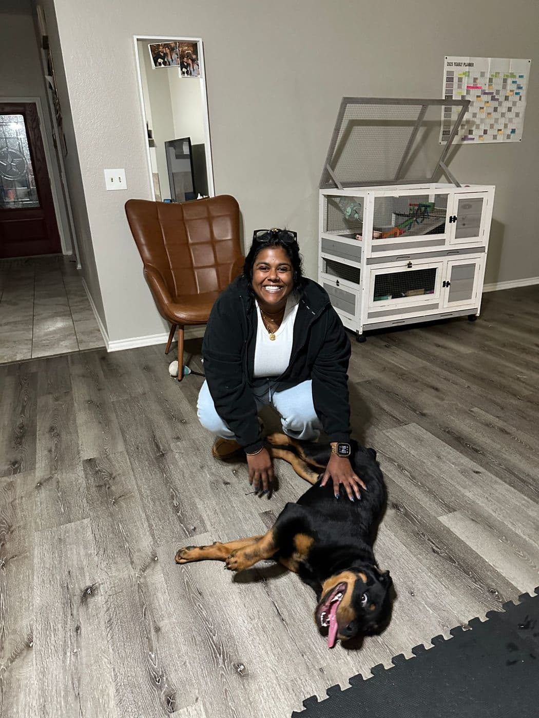 A Rottweiler relaxed on his back on the living room floor while his smiling owner gives him a belly rub